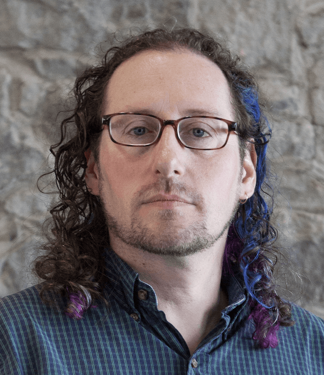 Author headshot. A White man in his 30s/40s with glasses and wisp of blue in his curly brown hair.